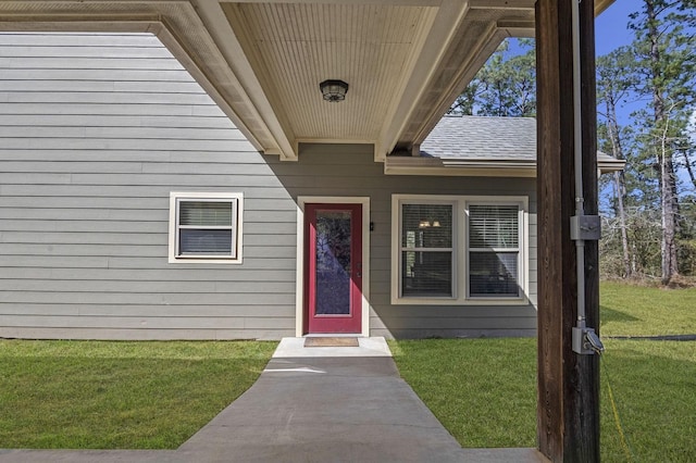 view of exterior entry featuring a yard and roof with shingles