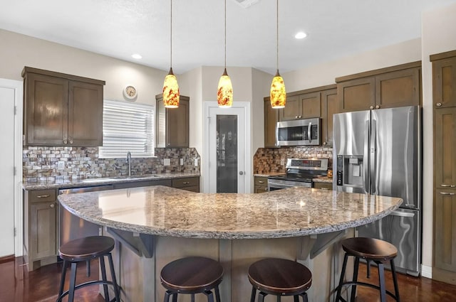 kitchen featuring tasteful backsplash, a breakfast bar, a center island, appliances with stainless steel finishes, and a sink