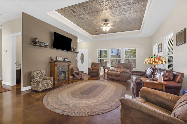 living room with baseboards, a raised ceiling, ceiling fan, a fireplace, and finished concrete floors