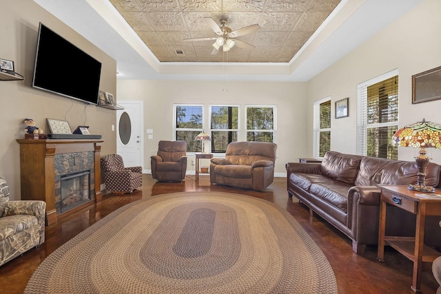 living room with a fireplace, visible vents, a tray ceiling, and a ceiling fan