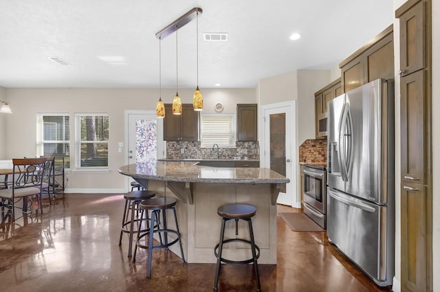 kitchen featuring concrete floors, a kitchen breakfast bar, backsplash, visible vents, and appliances with stainless steel finishes