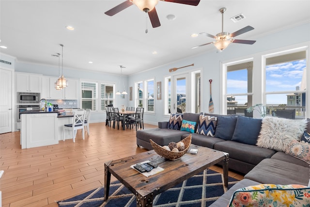 living room featuring light wood finished floors, ornamental molding, a ceiling fan, and visible vents