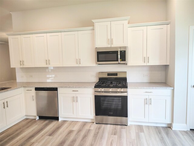 601 Greystone Ln, Angleton, TX 77515 - kitchen with stainless steel appliances, white cabinetry, backsplash, and light wood-style floors