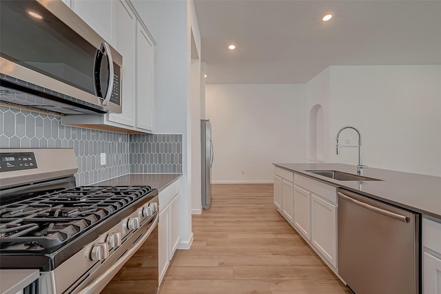 kitchen with decorative backsplash, white cabinetry, a sink, stainless steel appliances, and light wood finished floors