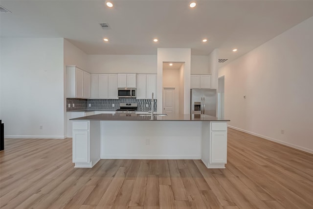 kitchen featuring visible vents, a sink, dark countertops, light wood-style floors, and stainless steel appliances