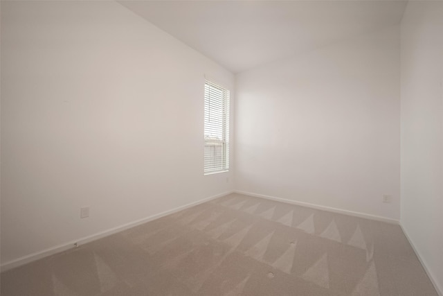 empty room featuring vaulted ceiling, light colored carpet, and baseboards