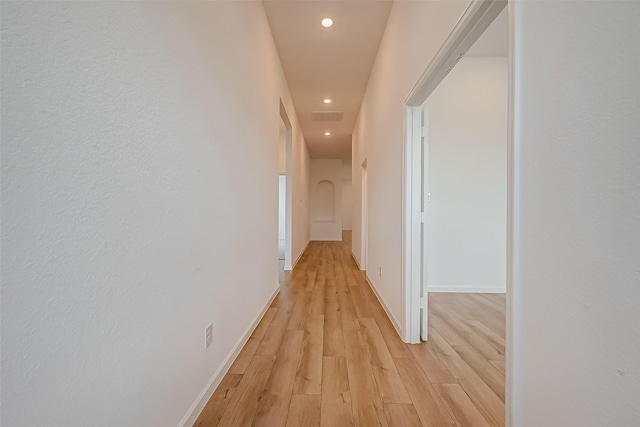 corridor with light wood-style floors, arched walkways, visible vents, recessed lighting, and baseboards