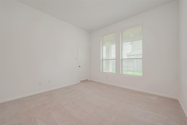 spare room with baseboards and light colored carpet
