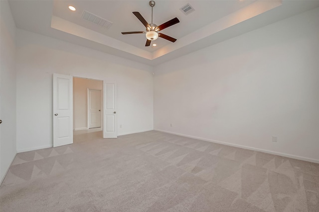 empty room featuring visible vents, a tray ceiling, and light carpet