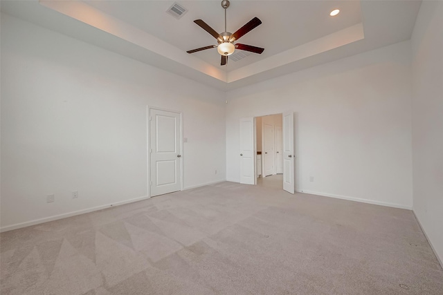unfurnished room featuring a raised ceiling, visible vents, light colored carpet, and ceiling fan