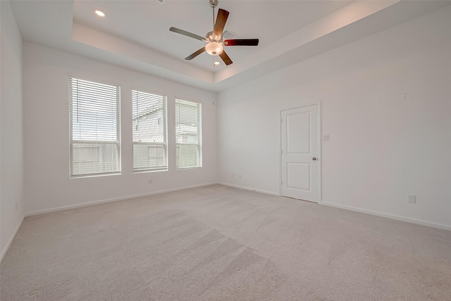empty room featuring a tray ceiling, light colored carpet, ceiling fan, and baseboards