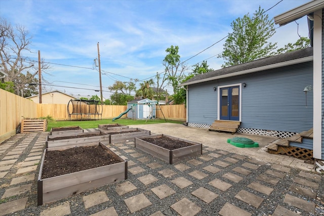 view of patio featuring a vegetable garden, a fenced backyard, entry steps, a playground, and a trampoline