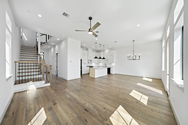 unfurnished living room featuring ceiling fan with notable chandelier, light wood-style flooring, visible vents, recessed lighting, and baseboards