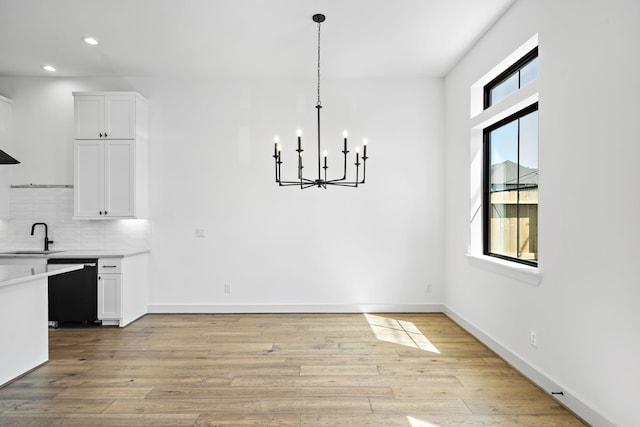 unfurnished dining area with recessed lighting, light wood finished floors, a notable chandelier, and a sink