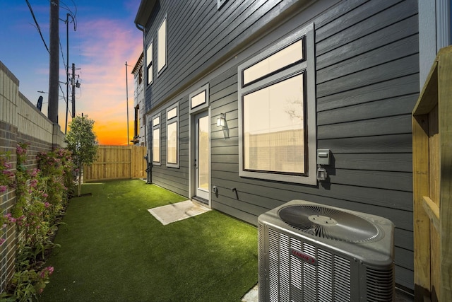 property exterior at dusk with central air condition unit, a yard, and a fenced backyard