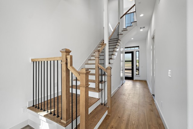 stairway featuring hardwood / wood-style floors, a high ceiling, and baseboards