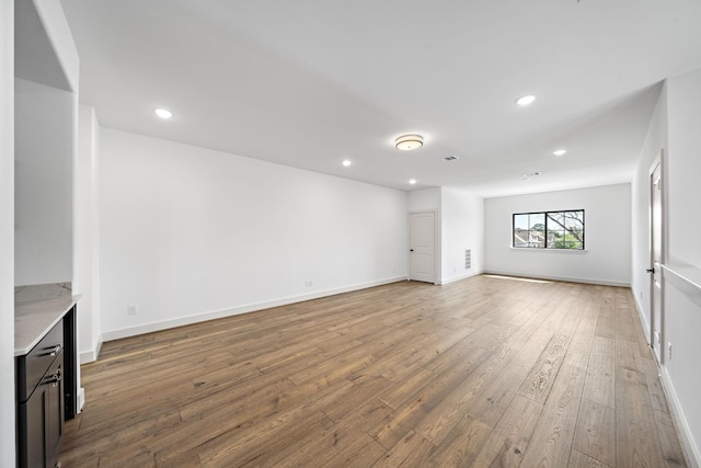 unfurnished living room with wood-type flooring, baseboards, and recessed lighting