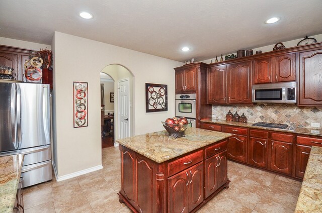 25419 Richton Falls Dr, Richmond, TX 77406 - kitchen with arched walkways, decorative backsplash, light stone counters, a kitchen island, and appliances with stainless steel finishes