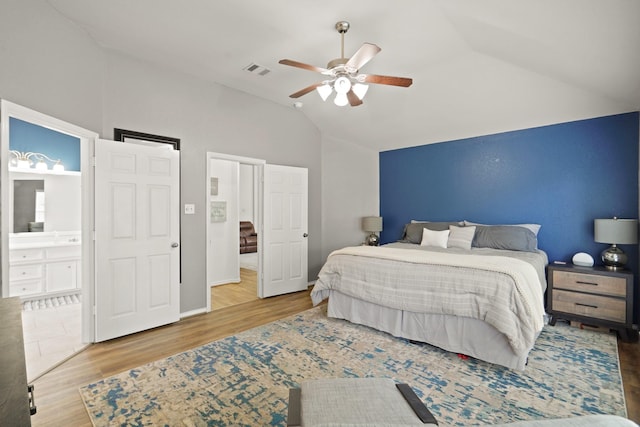 bedroom with lofted ceiling, wood finished floors, visible vents, a ceiling fan, and ensuite bath