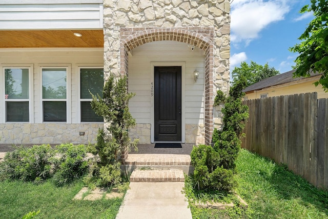 doorway to property featuring stone siding and fence