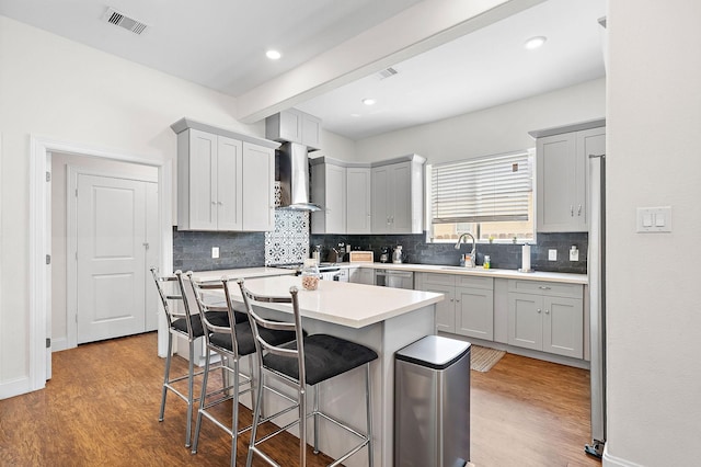 kitchen with a sink, a breakfast bar area, visible vents, wall chimney range hood, and wood finished floors