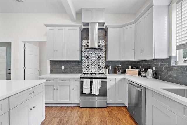 kitchen with appliances with stainless steel finishes, tasteful backsplash, wall chimney range hood, and light countertops