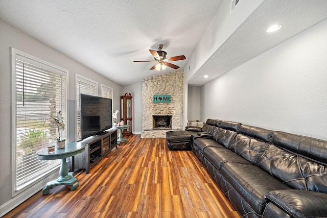 living room featuring a ceiling fan, a stone fireplace, visible vents, wood finished floors, and lofted ceiling