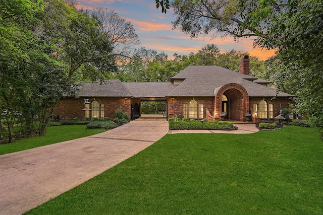 view of front of property with a front lawn, brick siding, a chimney, a shingled roof, and concrete driveway