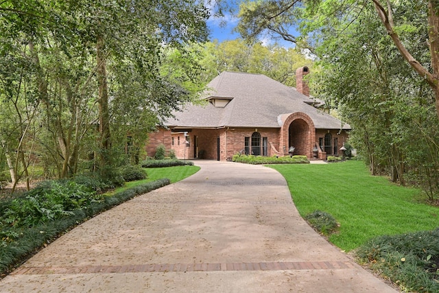 view of front of home featuring a chimney, brick siding, a front lawn, driveway, and roof with shingles