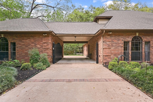 exterior space with a shingled roof, concrete driveway, and brick siding