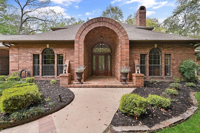 entrance to property featuring roof with shingles, brick siding, and a chimney