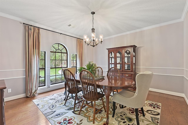 dining room with crown molding, visible vents, wood finished floors, a notable chandelier, and baseboards