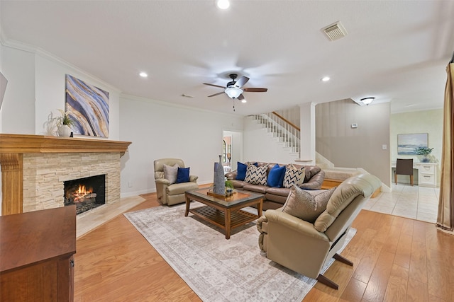 living room featuring ceiling fan, a fireplace, stairway, light wood finished floors, and baseboards