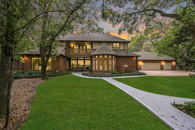 prairie-style home featuring a balcony, a front lawn, brick siding, a garage, and concrete driveway