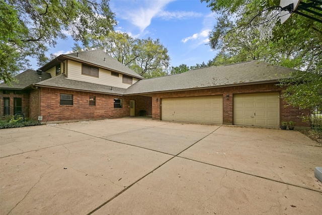 exterior space featuring an attached garage, roof with shingles, concrete driveway, and brick siding