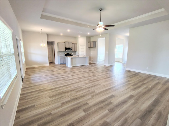 unfurnished living room with baseboards, recessed lighting, a ceiling fan, light wood-style floors, and a tray ceiling