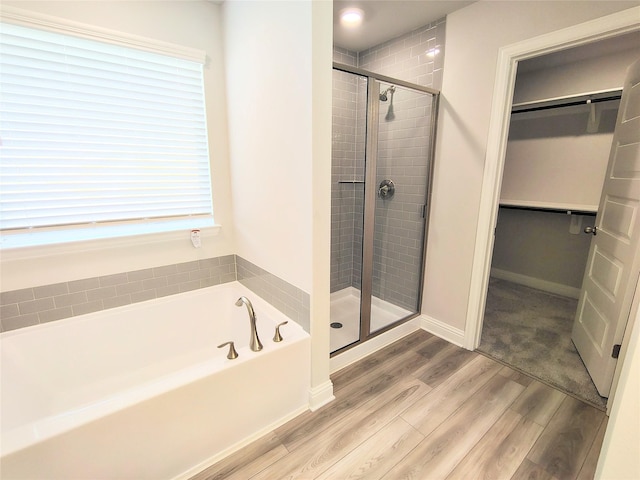 full bath featuring a bath, a stall shower, wood finished floors, and a spacious closet