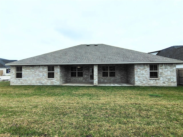 back of property with a yard, a shingled roof, brick siding, and a patio