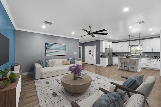 living area with light wood-style floors, baseboards, and ornamental molding