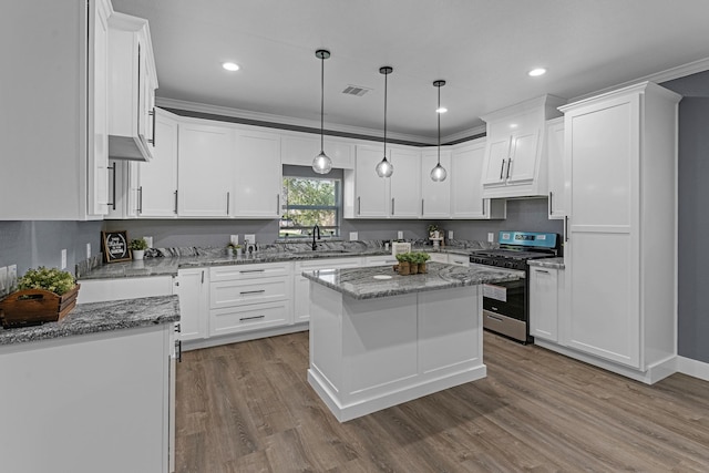 kitchen featuring stainless steel range with gas cooktop, white cabinets, visible vents, wood finished floors, and a sink