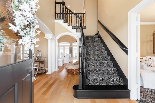 interior space featuring a towering ceiling, ornamental molding, stairway, decorative columns, and wood finished floors