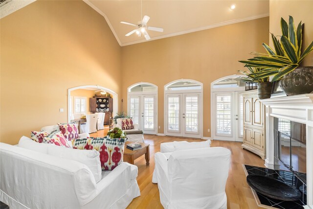 living room with ceiling fan, high vaulted ceiling, light wood-style flooring, ornamental molding, and a tiled fireplace