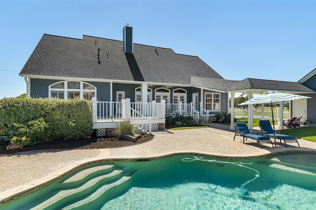 back of property with an outdoor pool, roof with shingles, a chimney, and a patio area