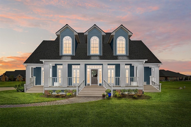 view of front of house featuring a front yard, a shingled roof, and covered porch