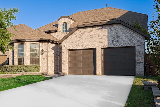 french country inspired facade featuring brick siding, a shingled roof, a garage, and driveway