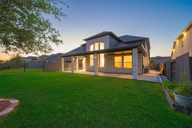 back of property at dusk with brick siding, a patio, a fenced backyard, and a lawn
