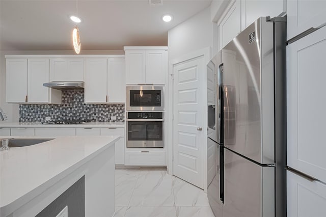 kitchen featuring white cabinets, a sink, under cabinet range hood, stainless steel appliances, and marble finish floor