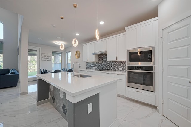 kitchen featuring under cabinet range hood, built in microwave, oven, marble finish floor, and a sink