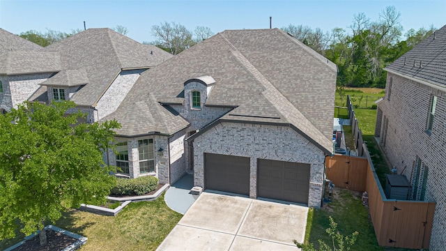 french provincial home with roof with shingles, stone siding, a front lawn, an attached garage, and driveway