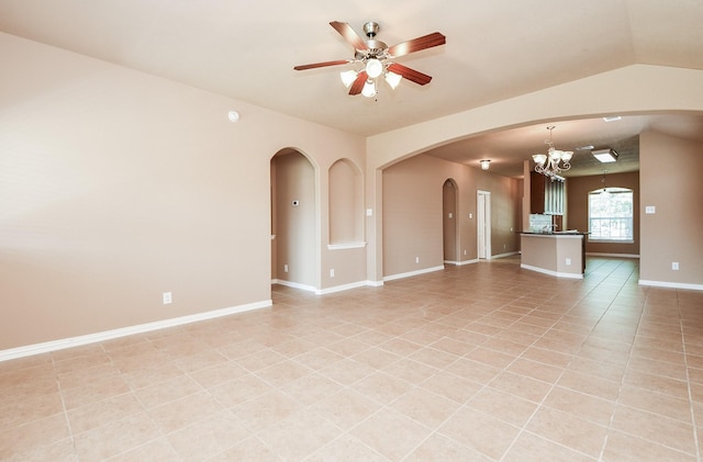 unfurnished living room with ceiling fan with notable chandelier, baseboards, arched walkways, and light tile patterned flooring